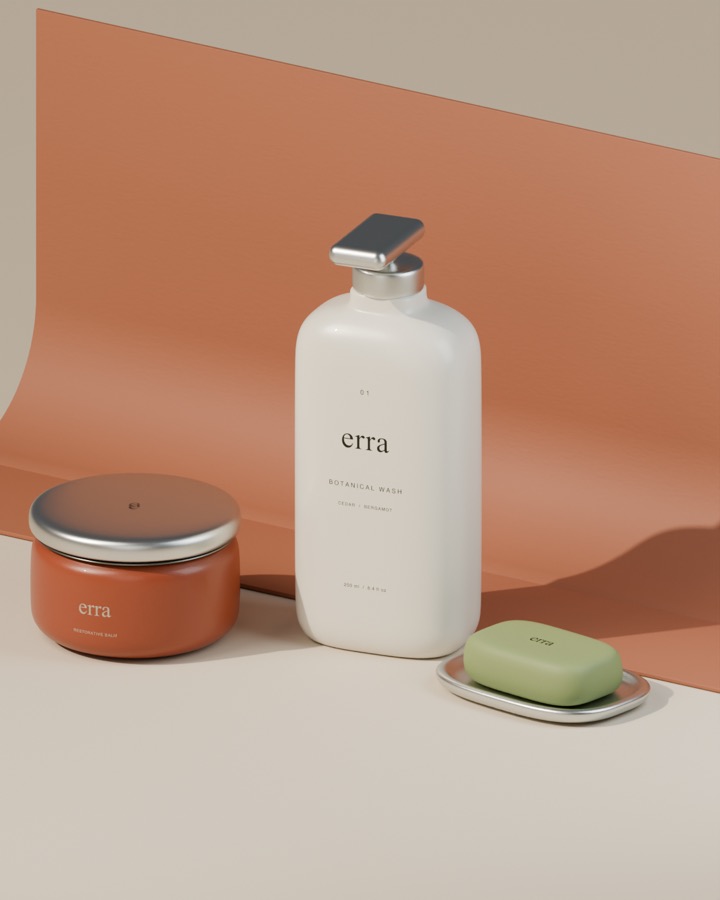 Art-directed set: an erra botanical wash bottle, balm jar and soap on a curved terracotta paper sweep with a hard sunlit shadow.